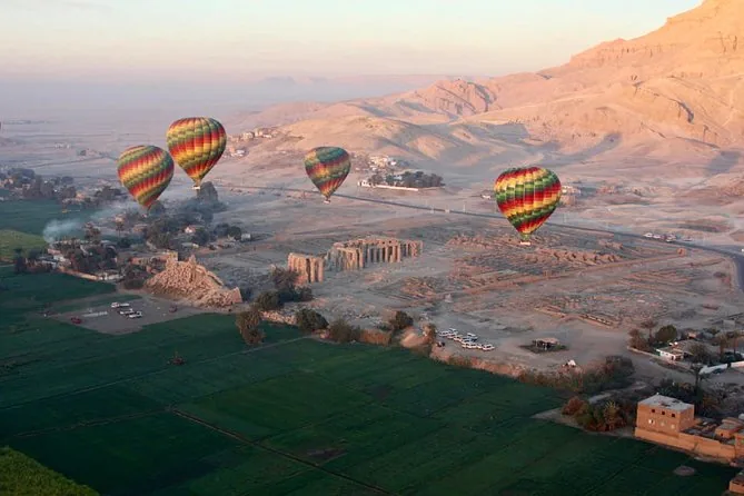 Diverse mongolfiere che si alzano sui campi verdi e sulla riva occidentale all'alba, con le colline del deserto dietro