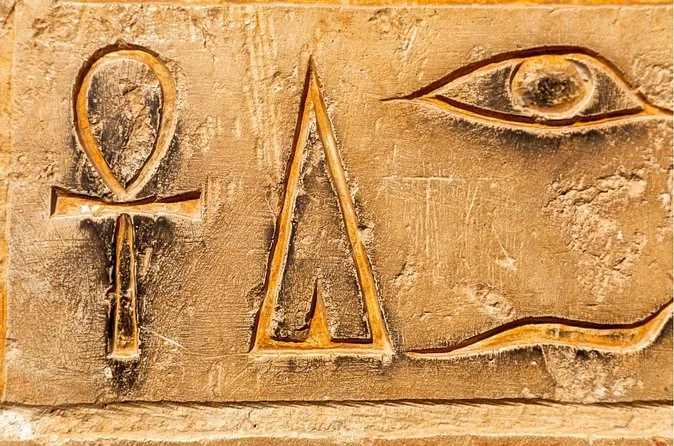 Ein Relief mit Anch, einem pyramidenförmigen Zeichen und einem Auge, hervorgehoben in goldfarbenem Stein