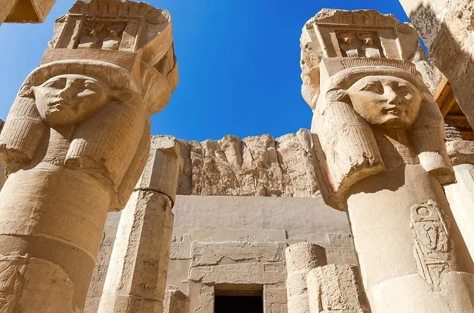 Zwei Pfeiler mit Hathor-Köpfen, Kuhohren und breiten Gesichtern vor blauem Himmel