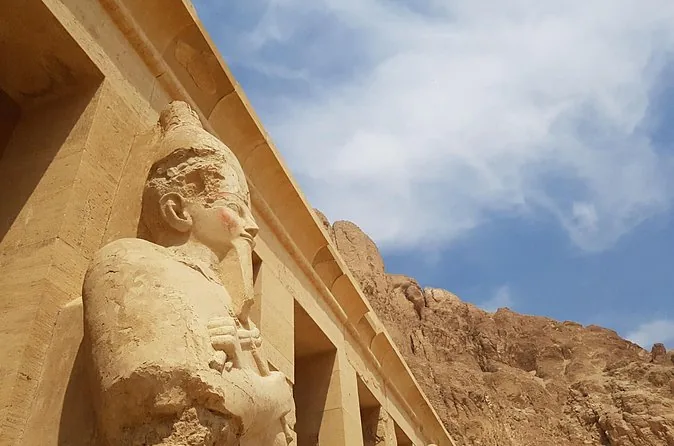 Nahaufnahme einer Osiris-Statue der Hatschepsut an einem Pfeiler, dahinter Felswand und Wolken