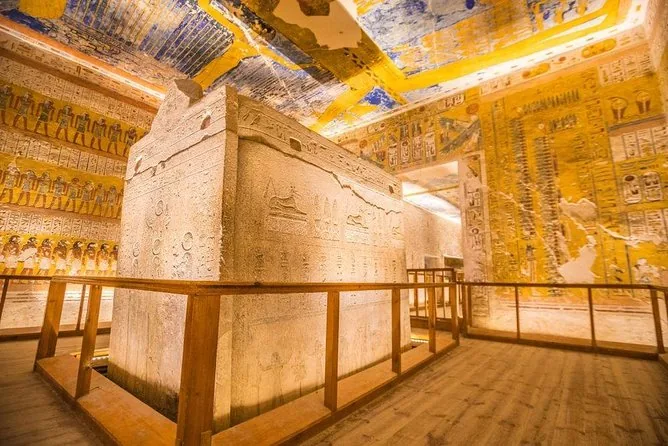 A painted burial chamber in the Valley of the Kings with a stone sarcophagus behind a wooden barrier