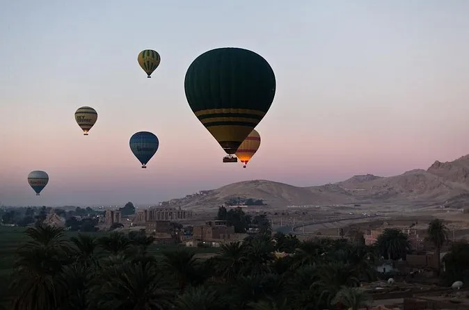 Diverse mongolfiere che si alzano in un cielo rosa all'alba sopra palme e colline scure