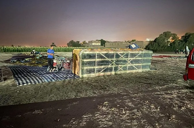 L'involucro di una mongolfiera steso a terra prima dell'alba accanto a un cesto, con l'equipaggio che si prepara